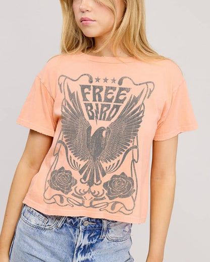 Woman wearing a peach t-shirt with a graphic design and blue jeans on a gray background