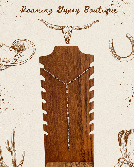 A wooden jewelry display stand holding a silver-toned chain necklace, centered on a vintage-style cream background with cowboy-themed illustrations and the text 'Roaming Lypsy Boutique' at the top.