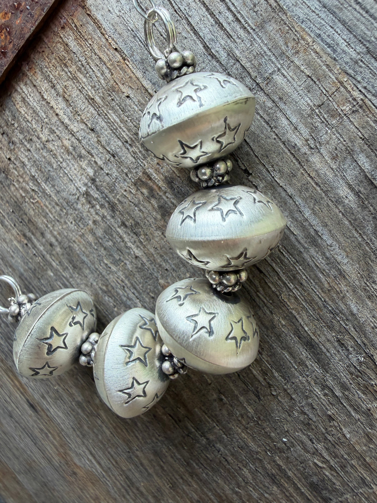 Sterling silver beaded jewelry featuring star-cut round beads and small metallic spacer beads, displayed on a rustic weathered wood surface. Monica Smith Pearl Necklace for sale
